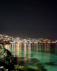 Illuminated city by sea against sky at night