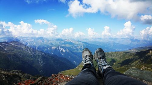 Low section of person relaxing on mountain against cloudy sky