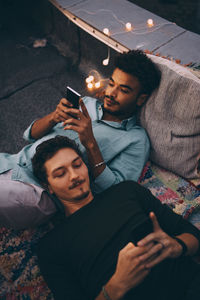 High angle view of male friends using smart phones while lying on terrace at dusk