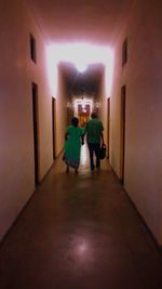 Rear view of people walking in illuminated corridor