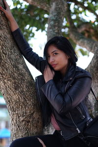 Portrait of young woman against tree trunk