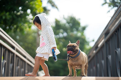 Girl standing with dog on footbridge against trees