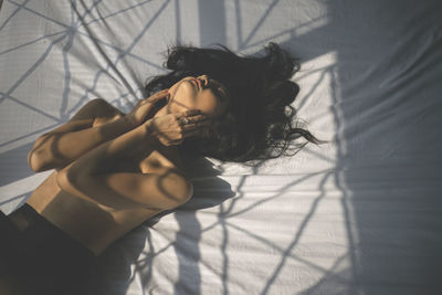 Sensual young woman lying down on bed during sunny day