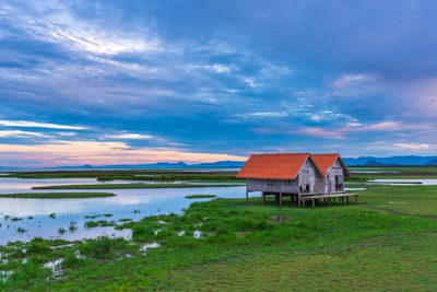 Houses at lakeshore against cloudy sky