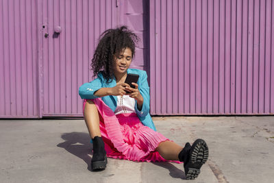 Young woman using mobile phone while sitting on laptop