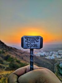 Close-up of hand holding sign against sky during sunset