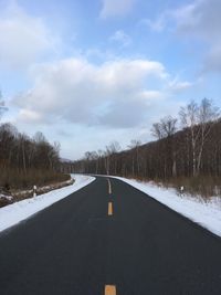 Road by snow covered landscape against sky