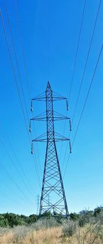 Low angle view of electricity pylon on field against clear blue sky