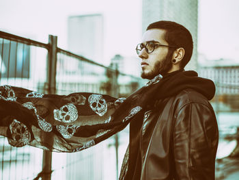 Thoughtful young man wearing scarf standing by railing in city