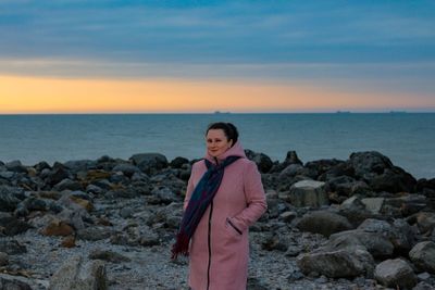 Woman standing on rock at beach against sky during sunset