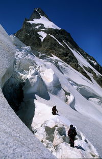 People climbing snowcapped mountain against clear sky