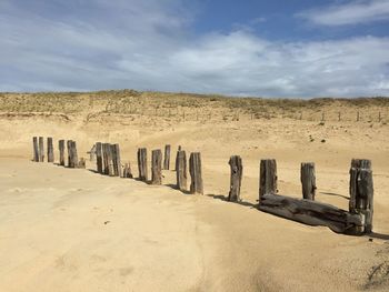 Wooden posts on sand against sky