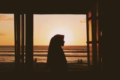 Silhouette woman looking at sea against sky during sunset