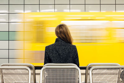 Rear view of woman sitting on bench at railroad station