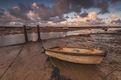 Boat moored at beach against cloudy sky