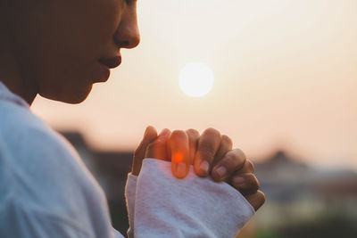Midsection of woman with hands clasped outdoors during sunset