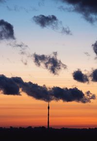 Silhouette of communications tower against cloudy sky