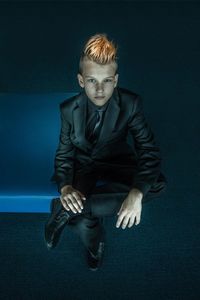 Portrait of boy in suit sitting against black background