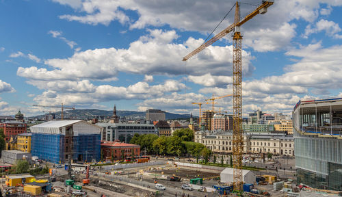 Low angle view of cranes against buildings in city