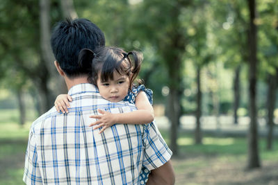 Rear view of father carrying cute daughter in park