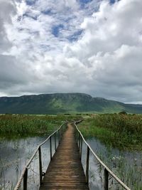 View of boardwalk on landscape against cloudy sky