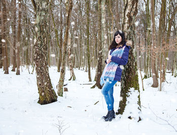 Portrait of woman standing against tree trunk on snow covered land