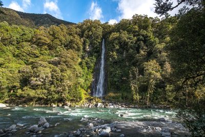 Scenic view of waterfall in forest against sky