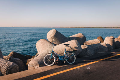 Bicycles on rock by sea against clear sky