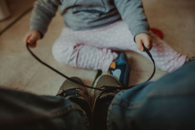 Low section of baby tying man shoelace on floor