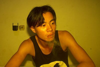 Young man looking away while smoking against wall