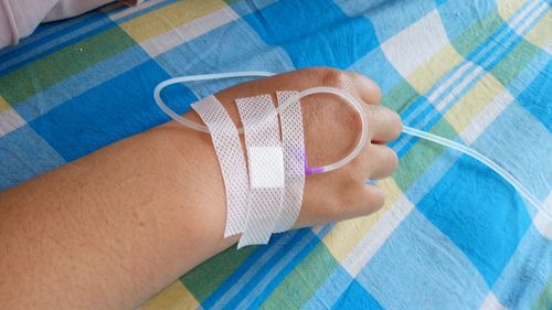 Close-up of hand with iv drip on bed at hospital