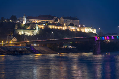 Illuminated bridge over river against buildings at night