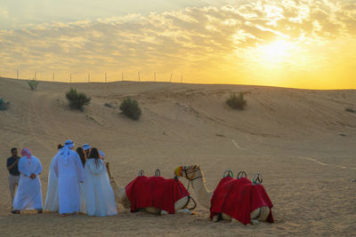 Rear view of people walking on desert during sunset