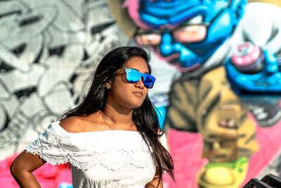 Portrait of young woman wearing sunglasses in front of grafti