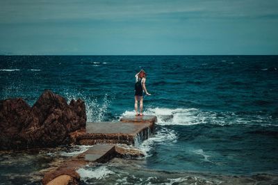 Man standing on rocks by sea against sky