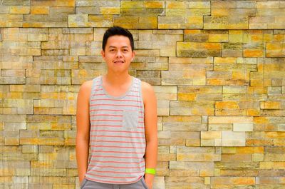 Portrait of a smiling young man standing against brick wall