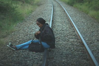Young woman with shoulder bag sitting on railroad tracks