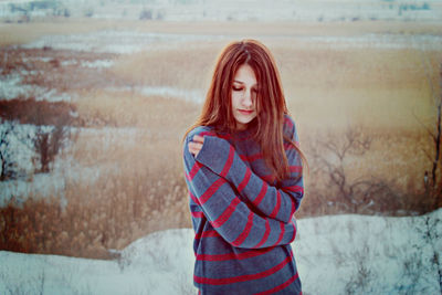 Young woman hugging self while standing on snow covered field