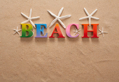 Directly above shot of beach text with seashells on sand at beach