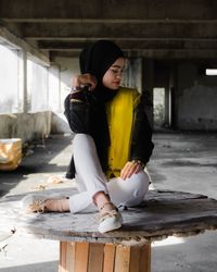 Woman wearing hijab while sitting on table in abandoned building