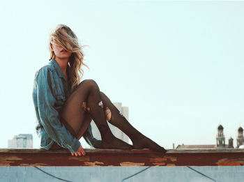 Young woman sitting against clear sky