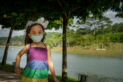 Little girl wearing face mask with rainbow dress enjoying outdoor in the park. new normal.