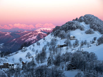 Scenic view of a village on a snow covered mountains against sky during sunrise