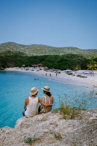 Rear view of people sitting at beach against clear sky