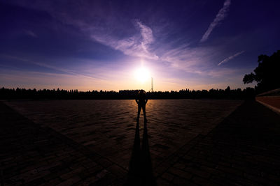 Silhouette person standing on footpath against sky during sunset