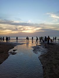 People on beach against sky during sunset