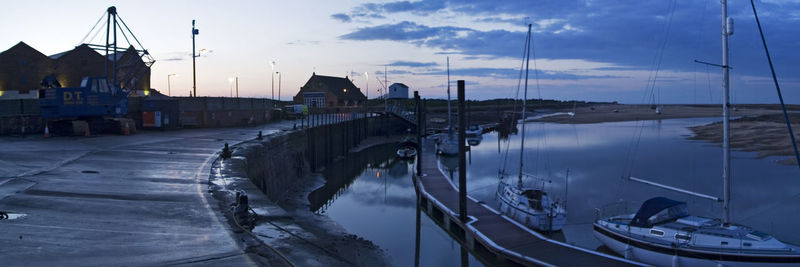 Sailboats moored on river in city against sky at dusk