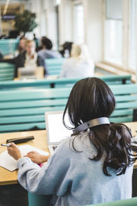 Rear view of young female students using laptop in cafeteria at university