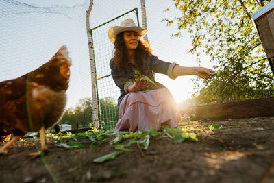 Woman farmer smiling feeding greens to free-range chickens on sunny farm