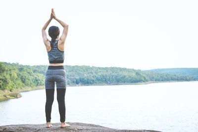 Rear view of woman standing by lake against clear sky